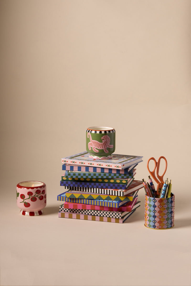 Notebooks stacked on top of each other next to pens and candles.