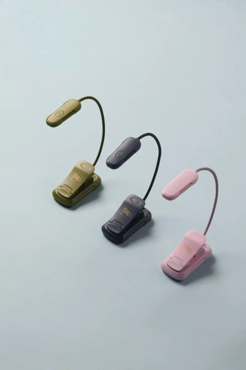 A compact and lightweight Book Light in lilac is displayed upright on a light blue surface, featuring 9 LED settings for customizable brightness.