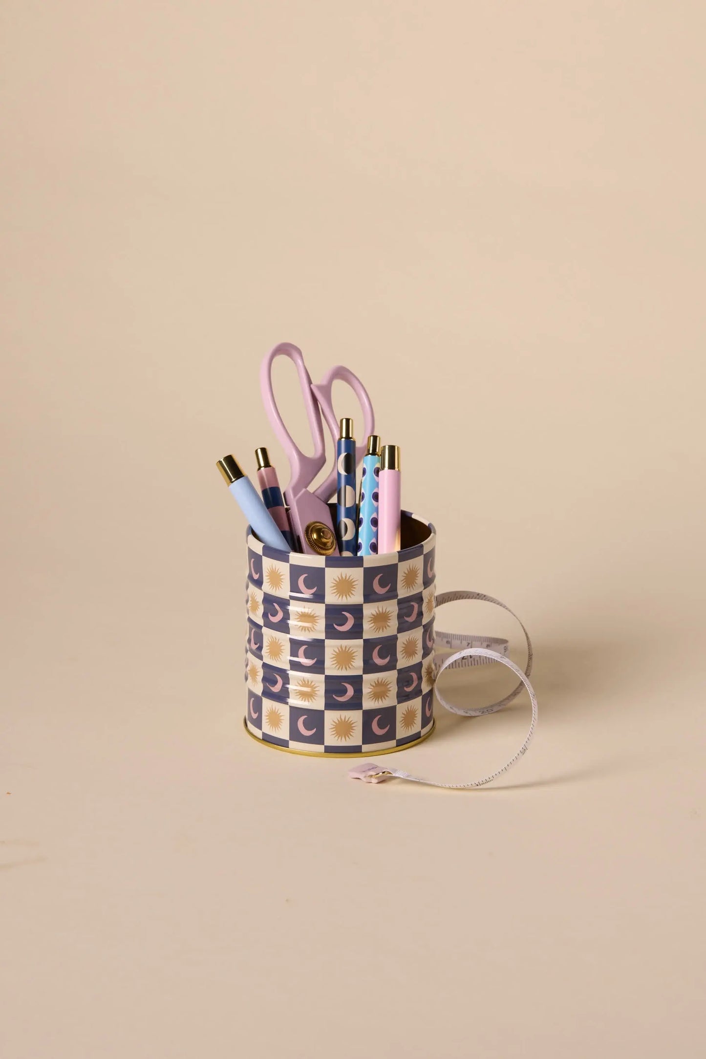 The A Dopo Celestial Storage Tin, adorned with pastel-hued pens, scissors, and a measuring tape, sits atop a plain beige background.