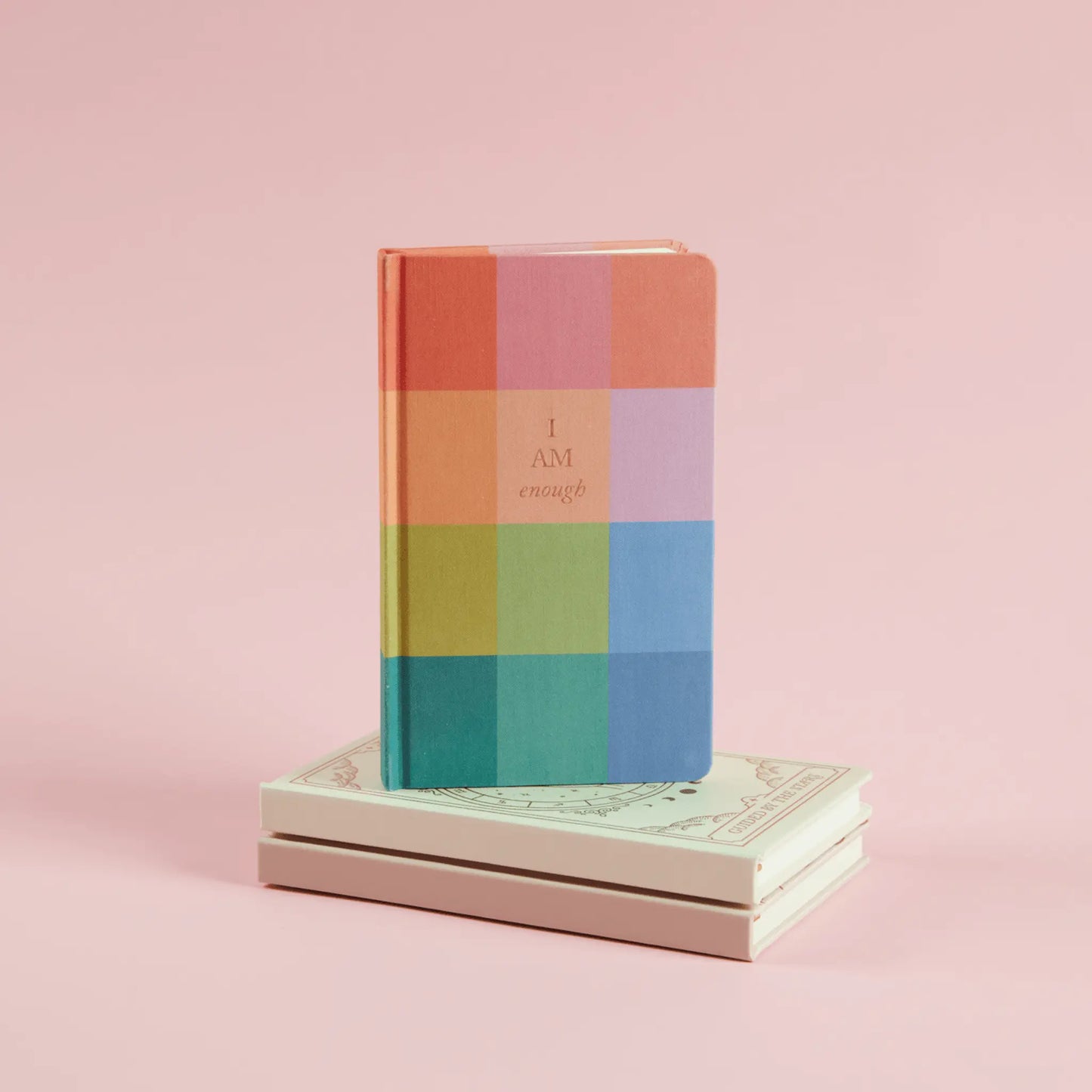 Rainbow check bookcloth journal resting on other journals with a pink background
