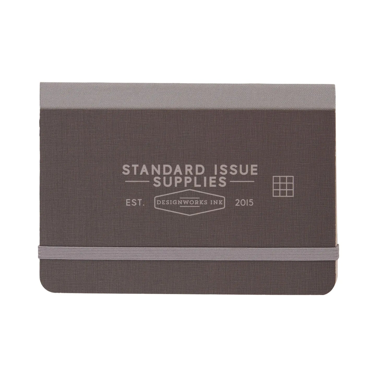 The Standard Issue Pocket Journal - Black is a compact journal with an elastic band closure, grid pages, and Standard Issue Supplies and Designworks Ink 2015 on the cover.