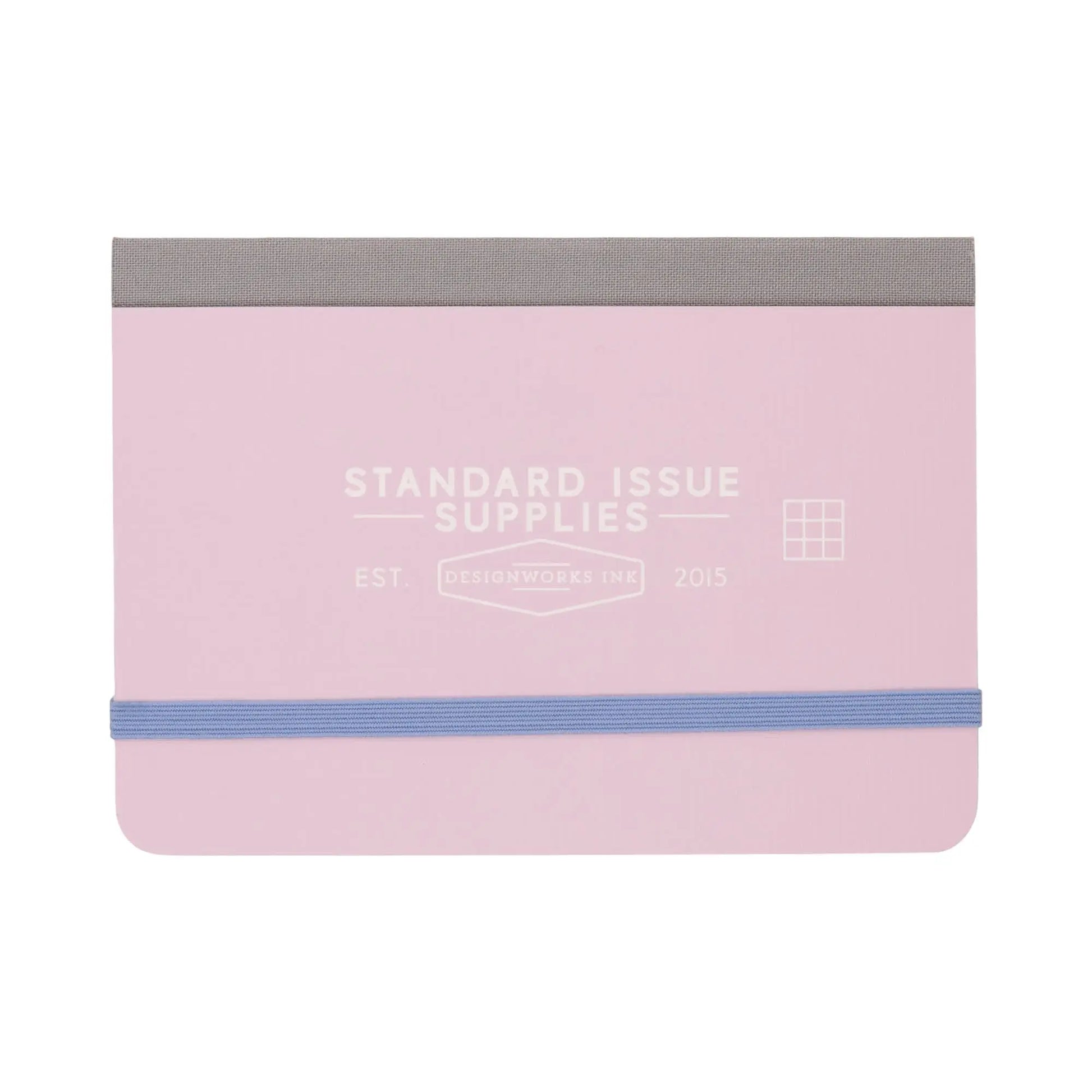 A compact Standard Issue Pocket Journal in lavender with a periwinkle elastic band and gray fabric spine, featuring Standard Issue Supplies on the cover. Includes grid pages inside for organized note-taking.