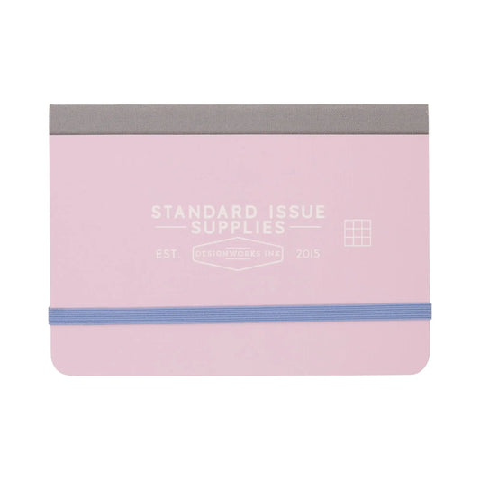 A compact Standard Issue Pocket Journal in lavender with a periwinkle elastic band and gray fabric spine, featuring Standard Issue Supplies on the cover. Includes grid pages inside for organized note-taking.