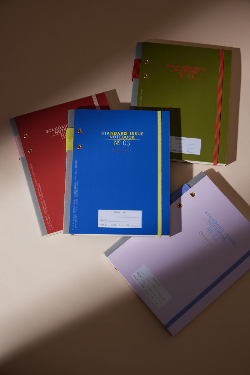 Four Standard Issue Planner Notebook No. 03 - Cobalt + Citron notebooks are arranged on a beige surface, their colorful covers and durable planner notebook design highlighted by soft lighting.
