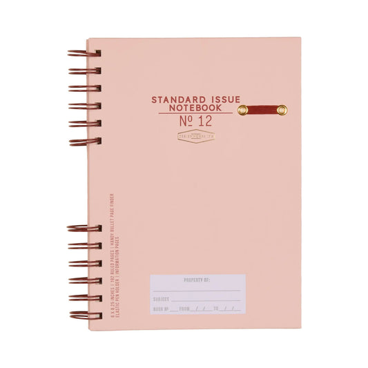 The Standard Issue Planner Notebook No. 12 - Rosewood + Blush is a pink, spiral-bound notebook with a small clasp and property label on the cover, crafted for a premium writing experience.