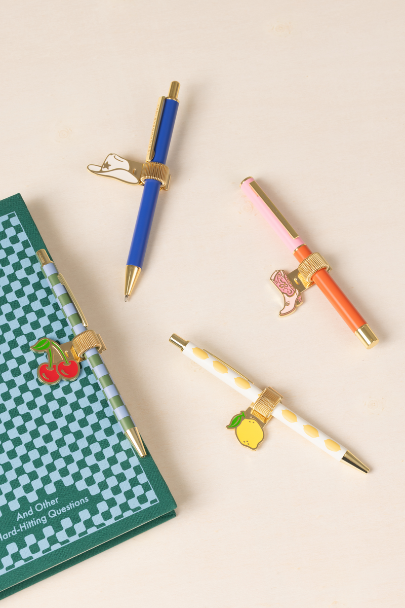Four pens with decorative pen charms on a beige background