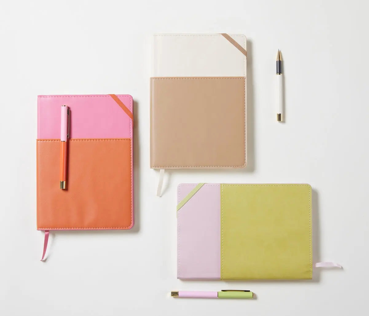 Three Journal + Pen Bundle (chili) sets, featuring color-blocked Vegan Leather Journals in orange-pink, beige-white, and yellow-lilac, are displayed on a white surface—each crafted from eco-friendly materials for sustainable style.