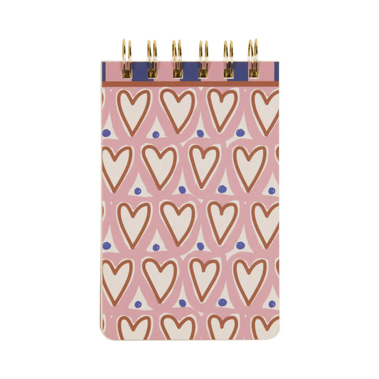 The A Dopo Hearts Twin Wire Notepad features a pink cover with white hearts outlined in brown and scattered blue dots, making it a charming addition to our whimsical collection.