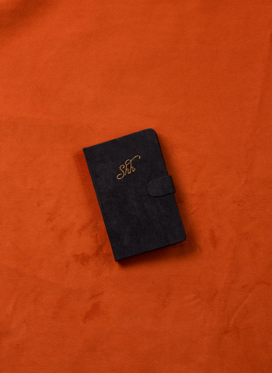 A closed black Mini Password Journal - Shh with gold lettering on the cover is set against an orange velvet fabric background.
