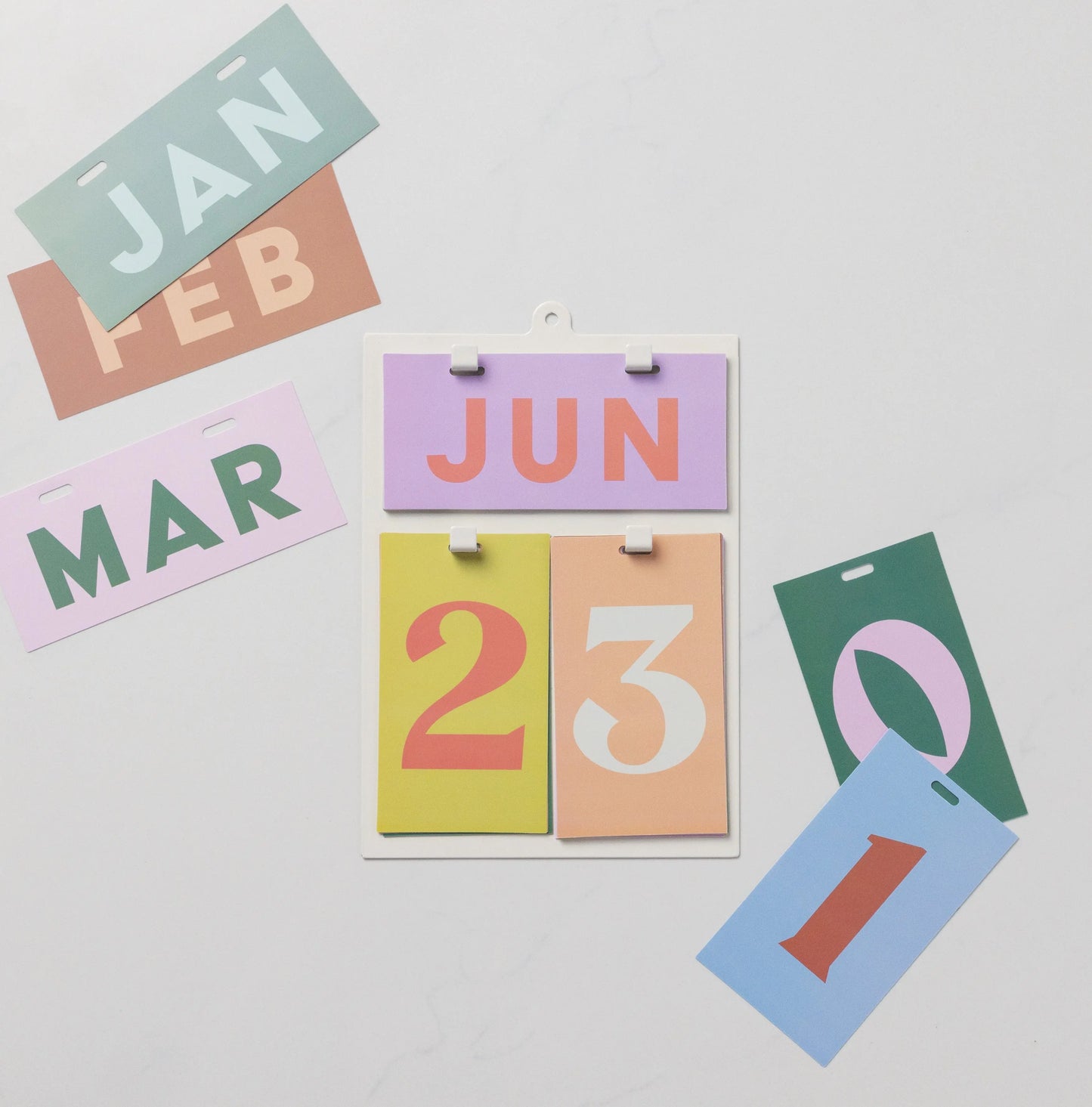The Perpetual Wall Calendar - Color Block features June 23 displayed, with colorful date cards scattered on a white surface—a modern twist on the classic calendar and a unique gift idea.