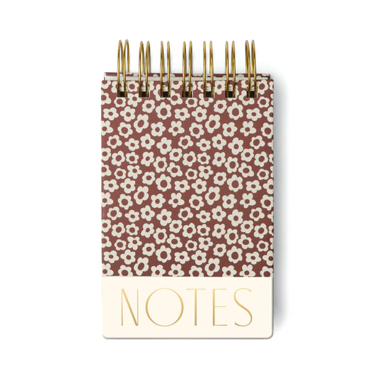 A chunky notepad with a burgundy cover featuring a groovy floral design and the words NOTES printed in large gold letters at the bottom.