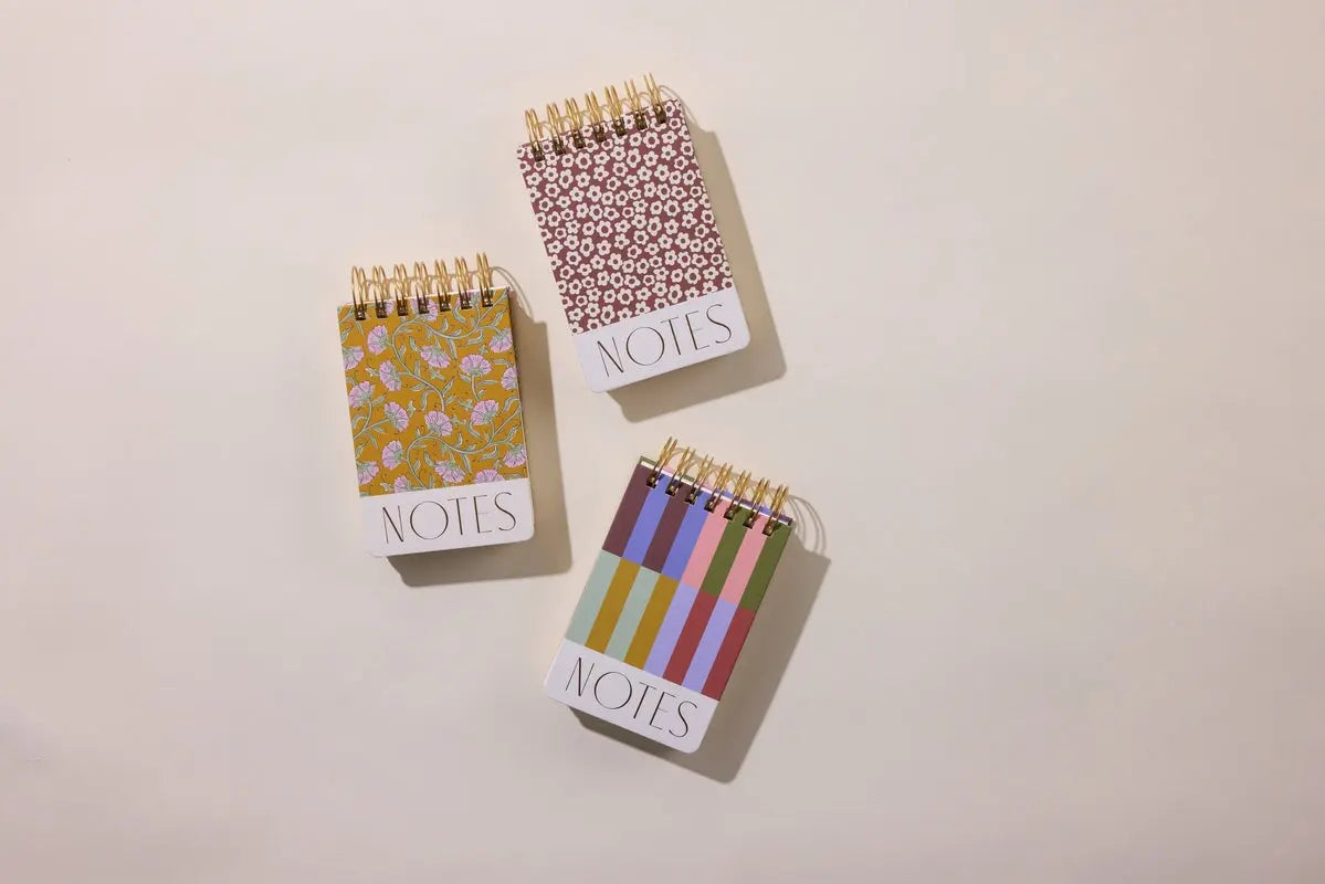 A chunky notepad with a burgundy groovy floral cover and NOTES on the front sits on a plain beige surface, showing off its unique spiral-bound design.