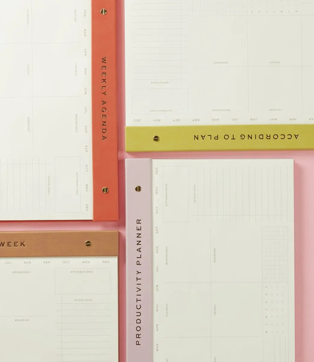 Four planners, including the Weekly Postbound Notepad - Lilac and a habit tracker, are displayed on a pink background. Each features colored spines with titles like WEEKLY AGENDA and PRODUCTIVITY PLANNER, inspiring organized productivity.