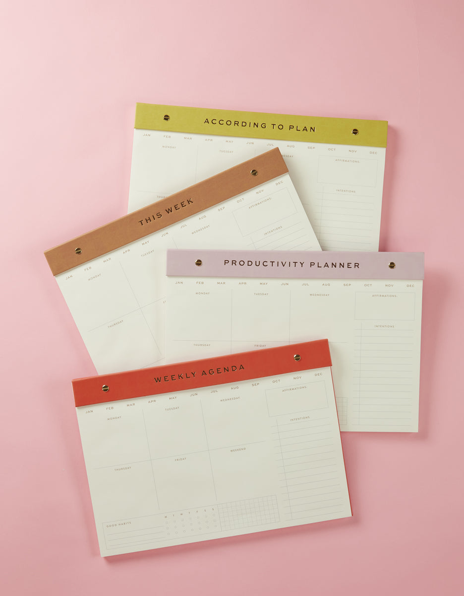 The Weekly Postbound Notepad - Camel is featured among four planners with green, brown, purple, and red headers on a pink background—labeled ACCORDING TO PLAN, THIS WEEK, PRODUCTIVITY PLANNER, and WEEKLY AGENDA—perfect for weekly tracking.