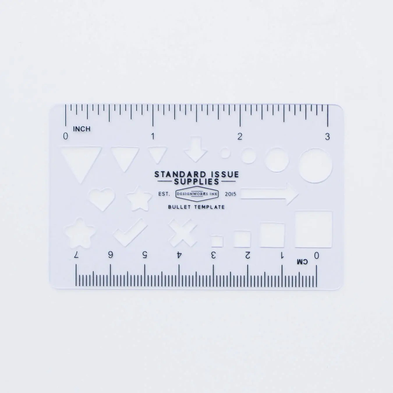 A transparent plastic template card with geometric shapes, rulers along the edges, and “Standard Issue Supplies” at its center—ideal for use with the Standard Issue Notebook No.3 - Black to enhance your writing experience.