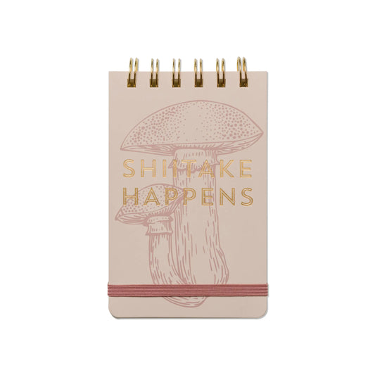 The Vintage Sass Notepad - Shiitake Happens features a beige cover with quirky shiitake mushroom art, gold SHIITAKE HAPPENS text, and a handy elastic band—perfect gift for any mushroom lover.