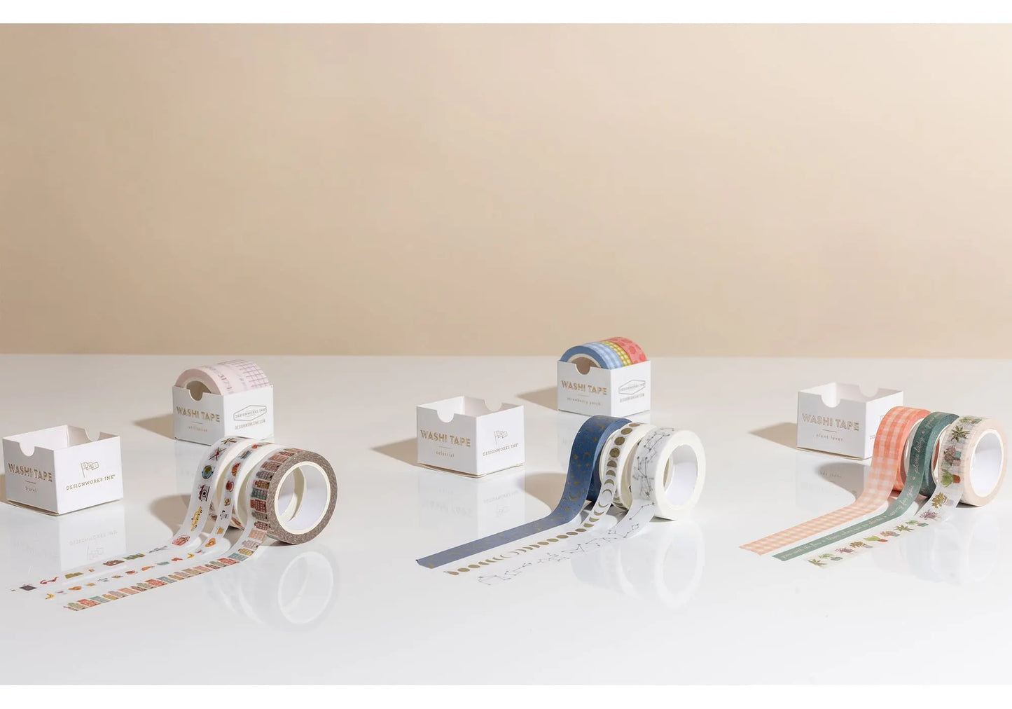Three rolls of decorative Washi Tape from the Travel set are displayed upright and unrolled on a reflective surface beside their packaging, ideal for scrapbooking or adding flair to your bullet journal.