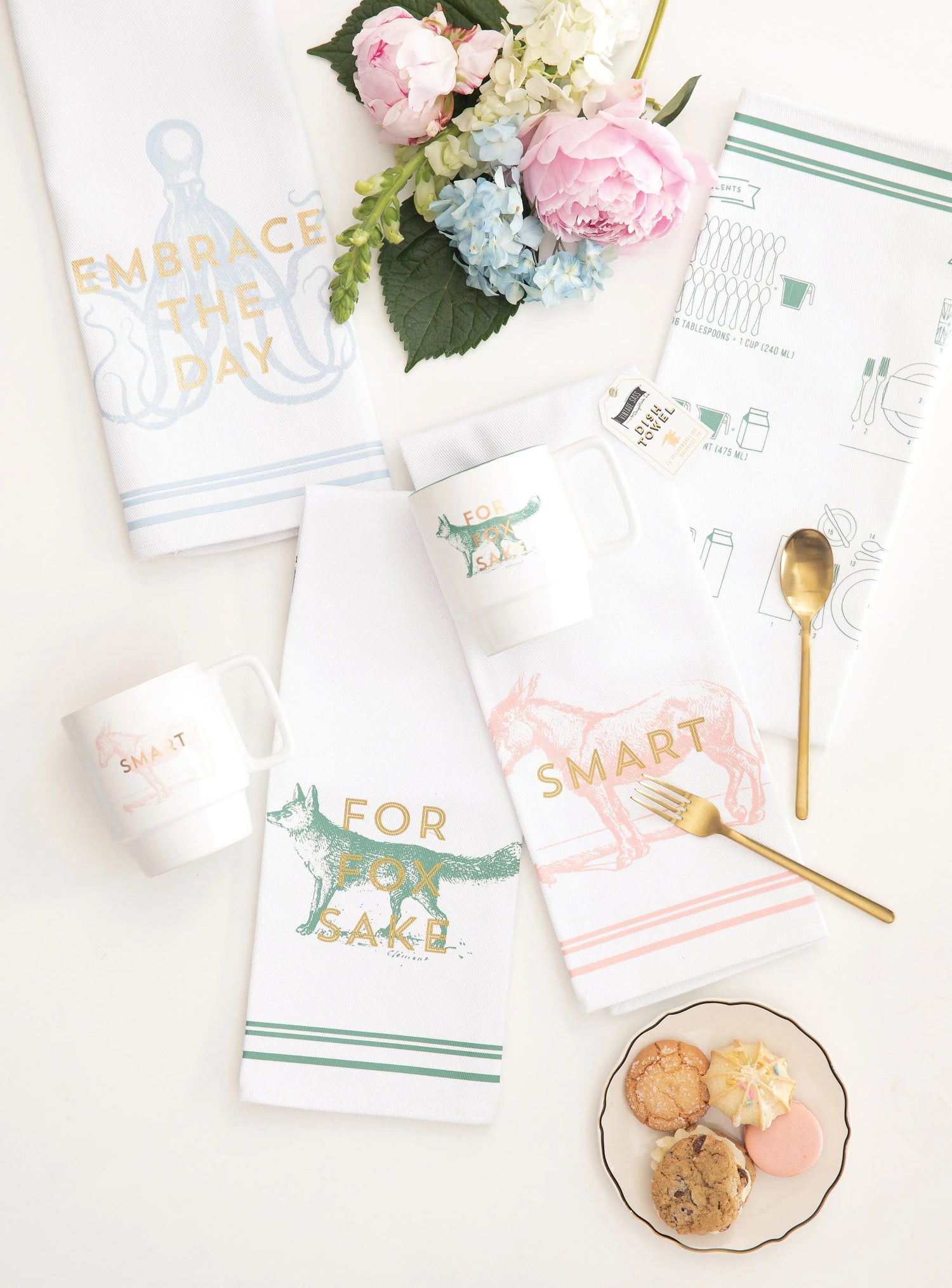 Mugs and dish towels next to flowers and cookies. 