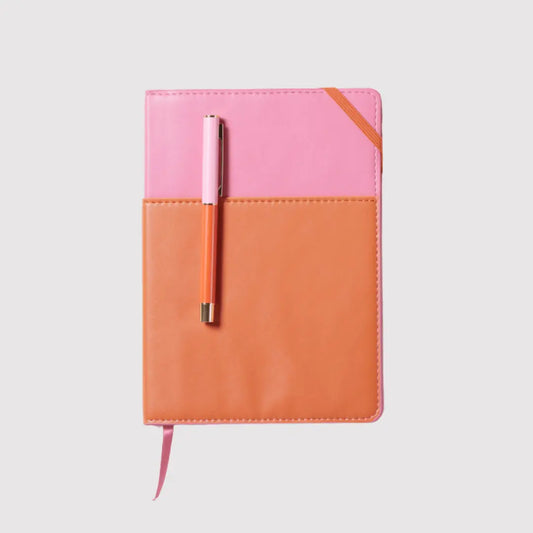 The Journal + Pen Bundle (chili)—a closed vegan leather pocket journal with a pink and orange cover and a matching pen clipped on top—rests on a plain light background.