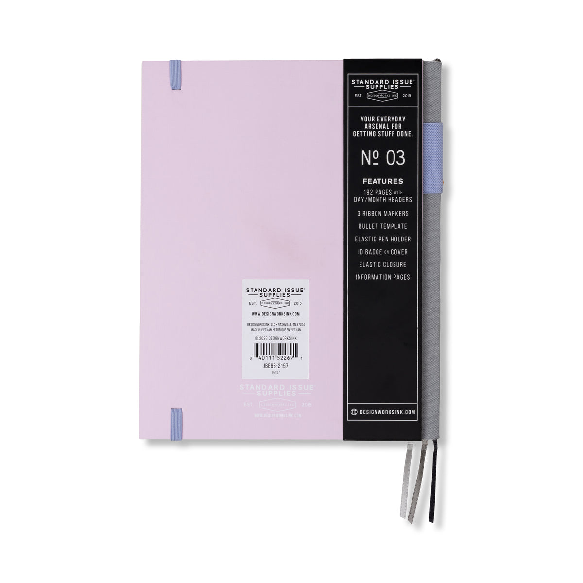 The Standard Issue Planner Notebook No. 03 - Lavender + Periwinkle is a closed, durable lavender notebook featuring a black band that highlights its features, such as two ribbon markers, a bullet template, an elastic pen holder, and an elastic closure, displayed against a white background.