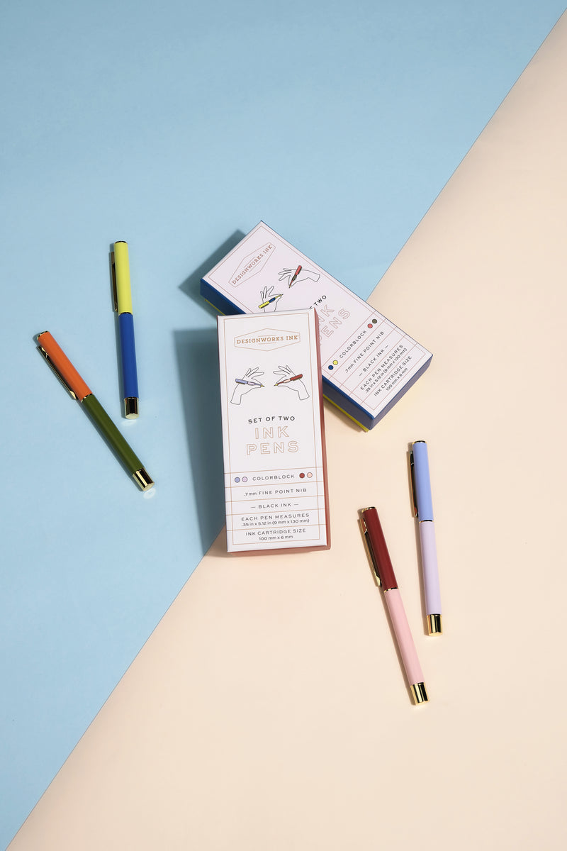 Five Color Block Pens in Cobalt + Army Green and two illustrated boxes labeled “Set of Two Ink Pens” with ultra fine ballpoint tips are arranged on a split blue and beige background.