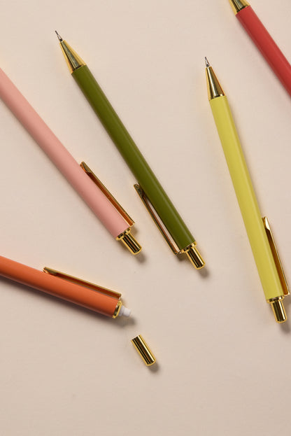 Five Mechanical Pencils - Cobalt + Citron with gold accents are arranged diagonally on a beige surface, blending pastel charm and precision. The orange pencil is uncapped, revealing its eraser—ideal for neat notes with a 0.7mm lead.