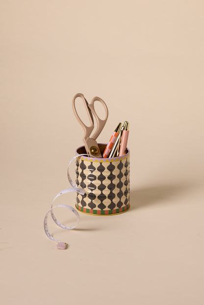 The A Dopo Black & White Wavy Storage Tin holds beige scissors, two pens, and a pencil, with a measuring tape draped over the edge, set against a plain beige background. Perfect for desk or jewelry storage.