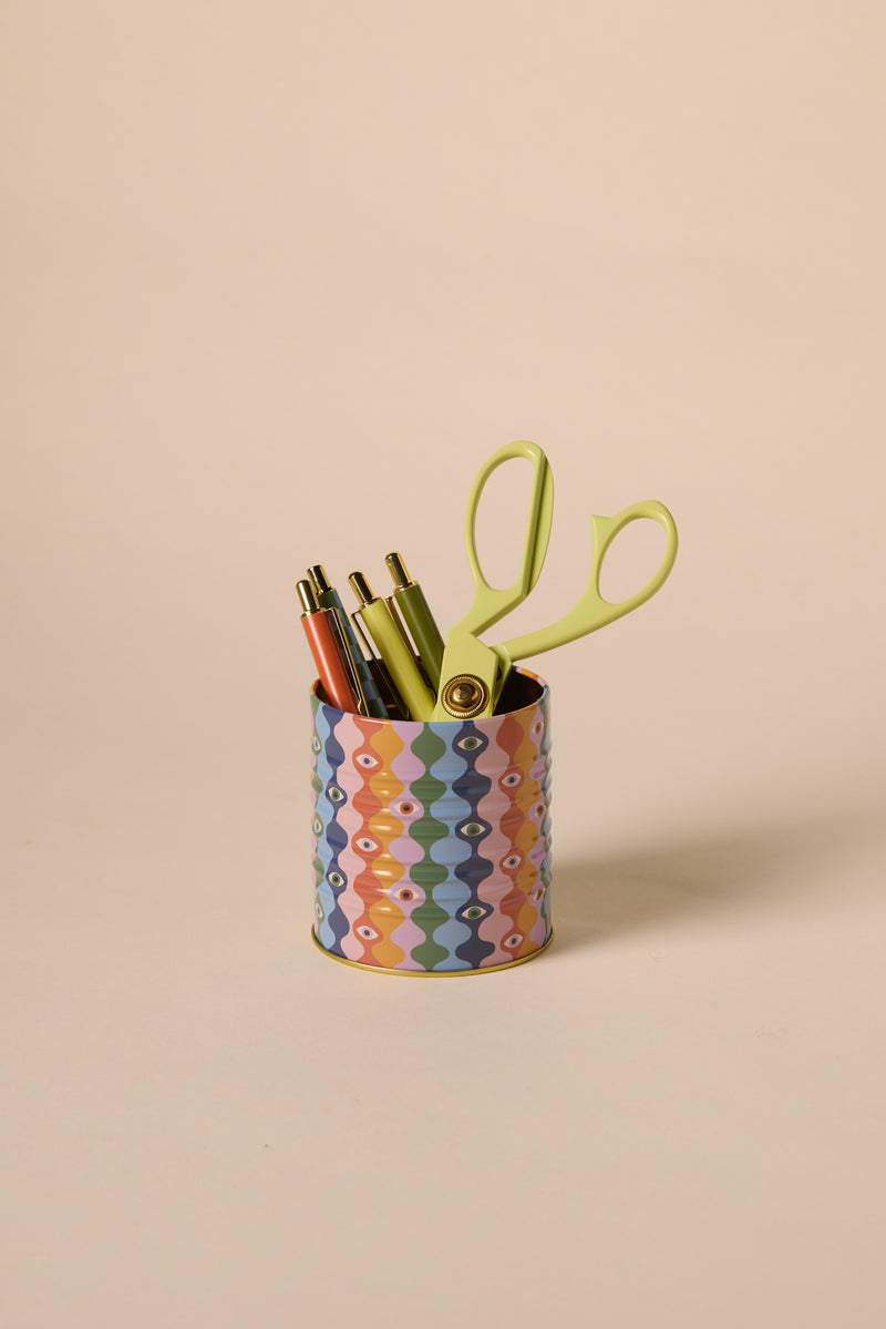 The A Dopo Eye Storage Tin, decorated with pastel patterns, holds three pens (orange, green, black) and light green scissors, displayed against a plain beige background.