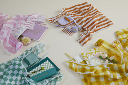 Four Reusable Market Bag - Checkered bags in pink, orange, green, and yellow hold notebooks, pens, water bottles, and flowers, all neatly arranged on a light surface.