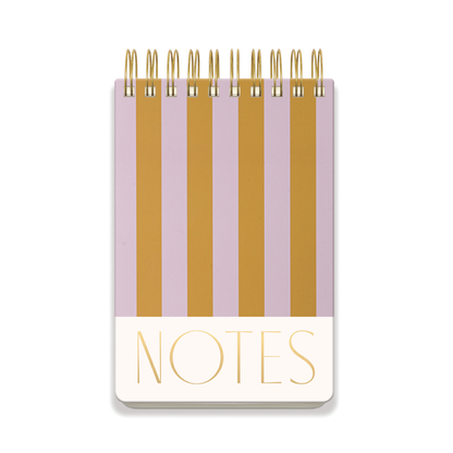 The Chunky Large Twin Wire Notepad features a hard cover with vertical lilac and ochre stripes, lined sheets for easy writing, and "NOTES" printed in bold gold letters at the bottom of the cover.