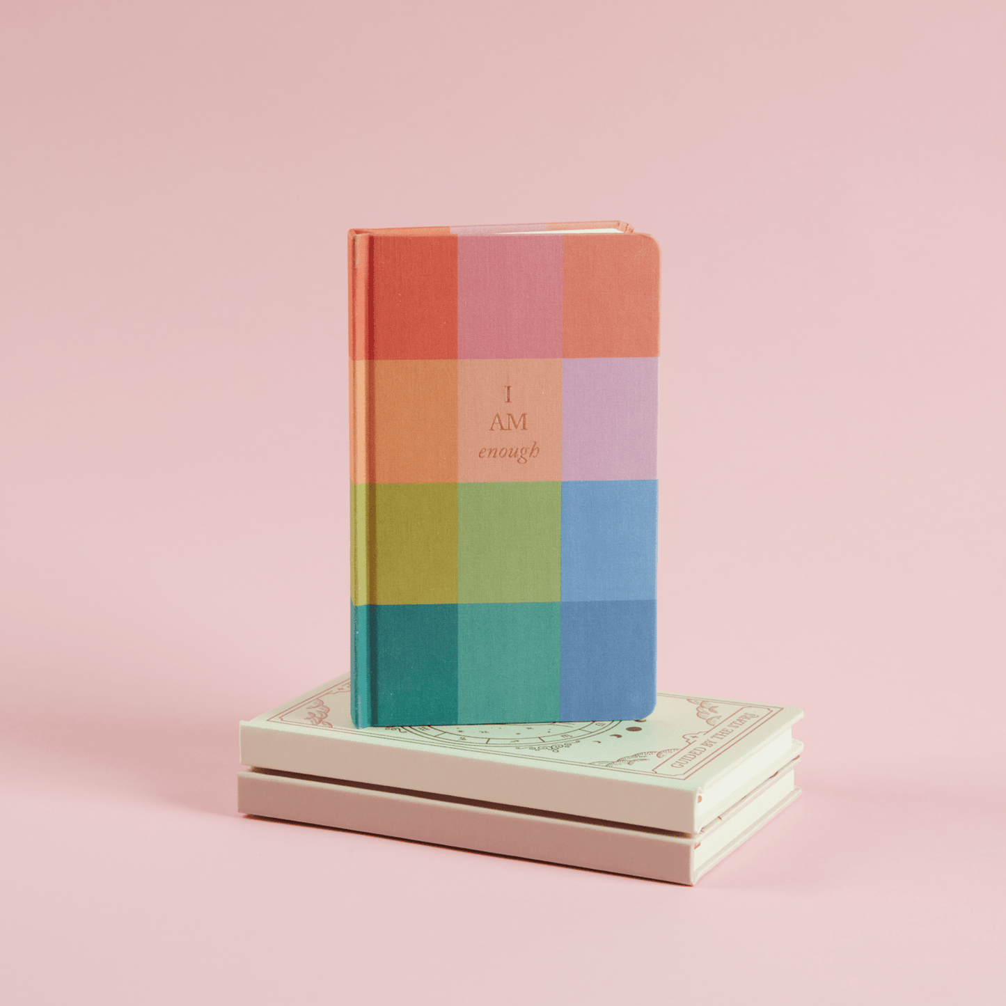 Rainbow check bookcloth journal resting on other journals with a pink background