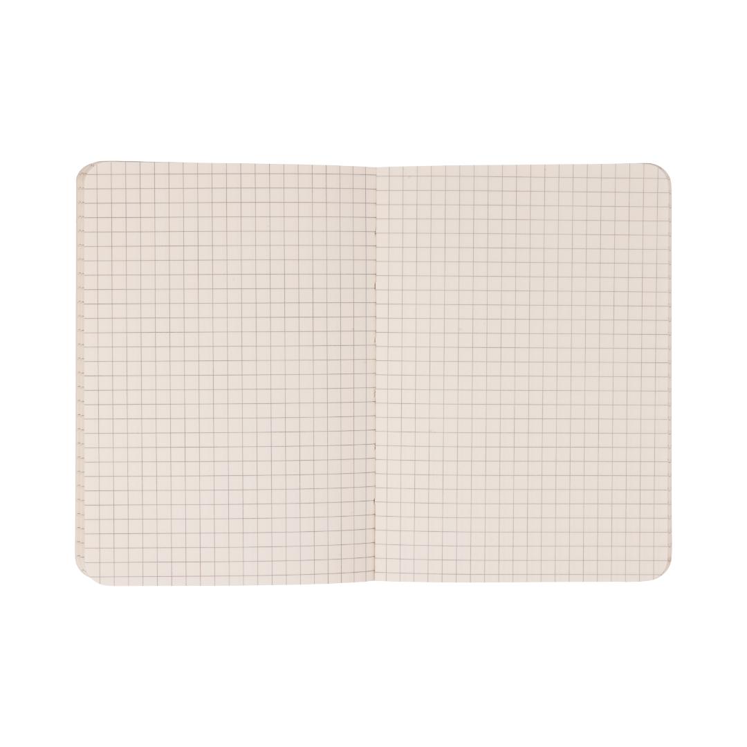 The Standard Issue Pocket Journal - Black features squared graph paper pages with a clear grid pattern, making it ideal for use as a travel journal or pocket notebook. Photographed from above against a white background, the open notebook highlights its distinctive design.