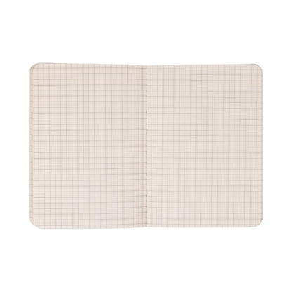 The Standard Issue Pocket Journal - Black features squared graph paper pages with a clear grid pattern, making it ideal for use as a travel journal or pocket notebook. Photographed from above against a white background, the open notebook highlights its distinctive design.
