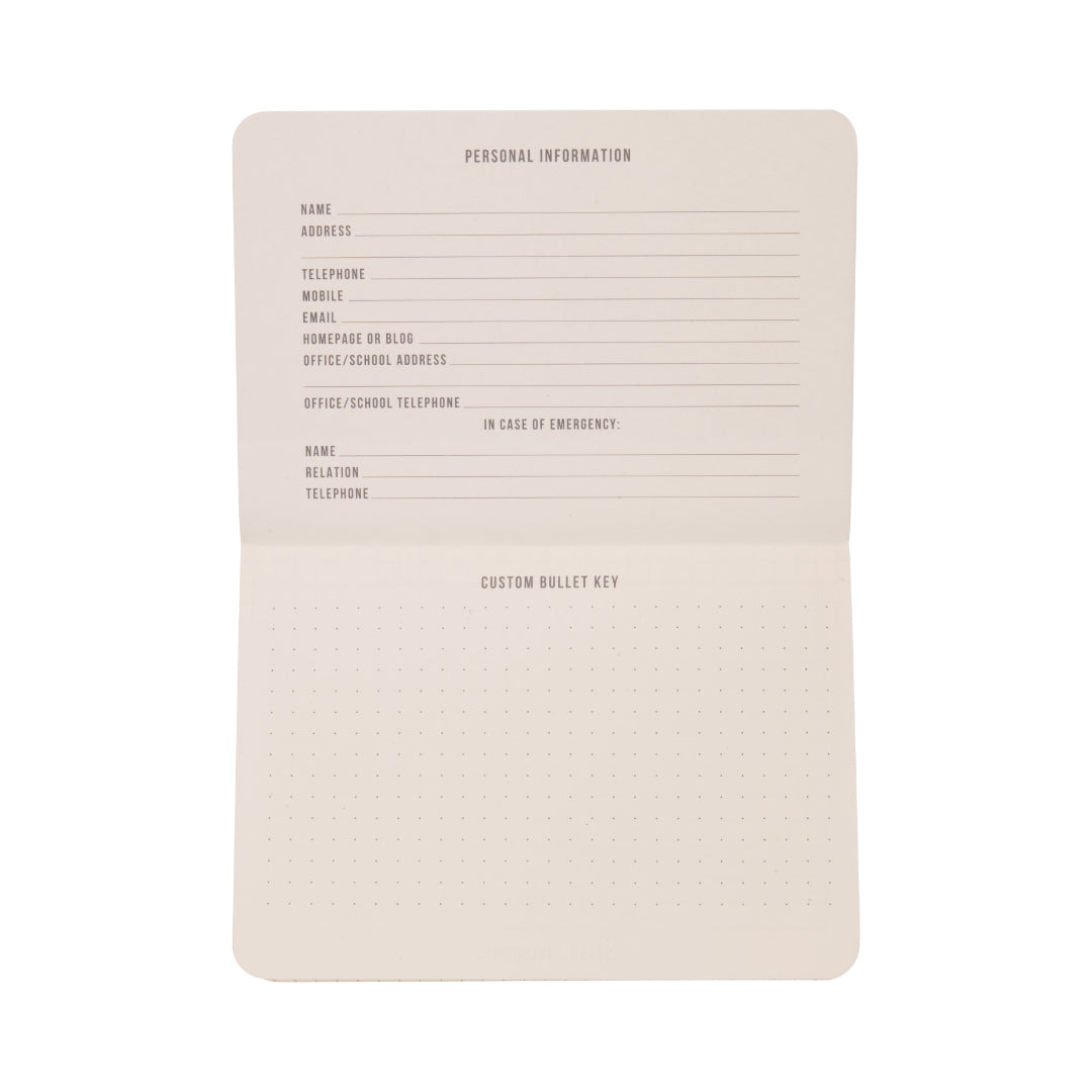 The Standard Issue Pocket Journal - Rosewood + Blush features an open grid design with dedicated sections for personal information and emergency contacts on the top page, while the bottom page offers a dotted grid ideal for creating a custom bullet key. Perfect as a pocket journal or travel notebook, its pages remain blank apart from printed labels.