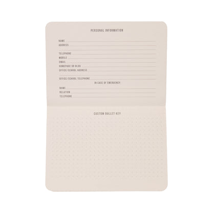The Standard Issue Pocket Journal - Rosewood + Blush features an open grid design with dedicated sections for personal information and emergency contacts on the top page, while the bottom page offers a dotted grid ideal for creating a custom bullet key. Perfect as a pocket journal or travel notebook, its pages remain blank apart from printed labels.