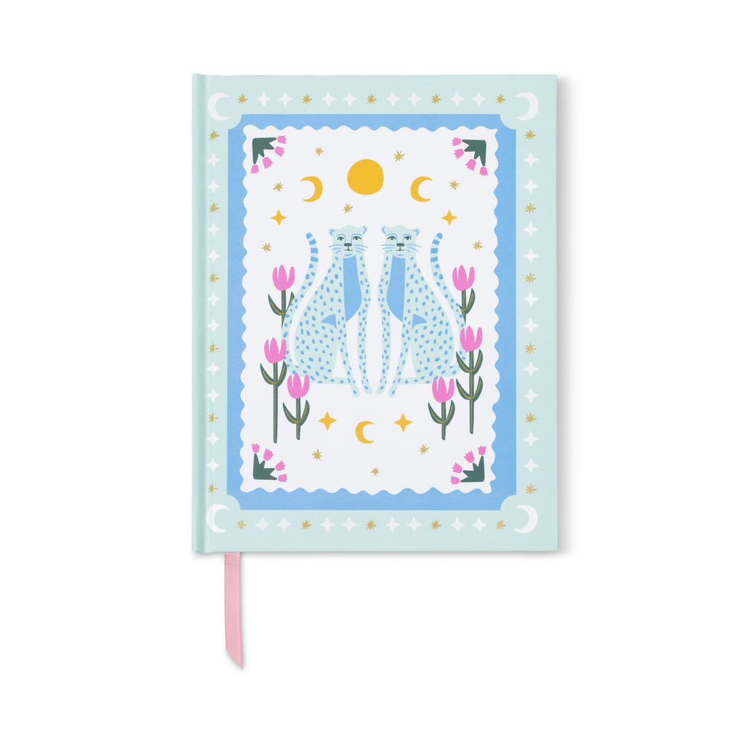 The A Dopo Blue Cheetah Journal features a light blue cover illustrated with two blue cheetahs sitting back to back amid pink flowers, crescent moons, stars, and a sun. Crafted with eco-friendly materials and a lay-flat binding for comfortable writing, it also includes a pink ribbon bookmark visible at the bottom.