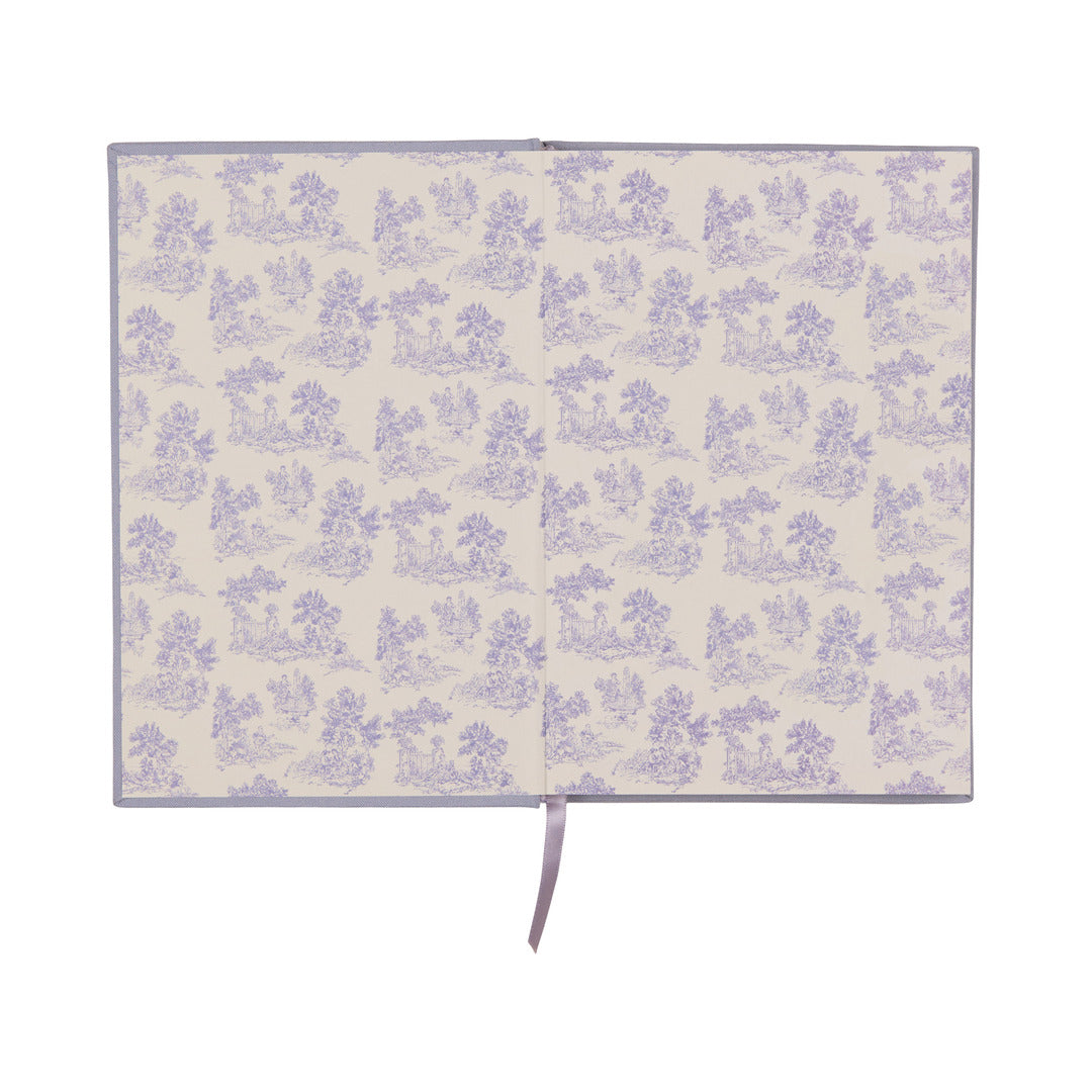 An open book reveals patterned endpapers featuring a repeating light purple floral and pastoral scene on a cream background, with a lavender ribbon bookmark draped down the center. The Very Tired Woman Journal showcases a bookcloth cover and lay-flat binding for effortless writing or sketching across its pages.