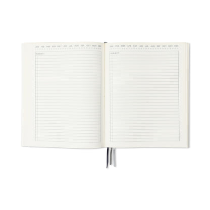 The Standard Issue Planner Notebook No. 03 - Rosewood + Blush is open to lined pages labeled SUBJECT with months across the top. Two rosewood and blush ribbon bookmarks can be seen at the bottom, and the pages are ready for writing.