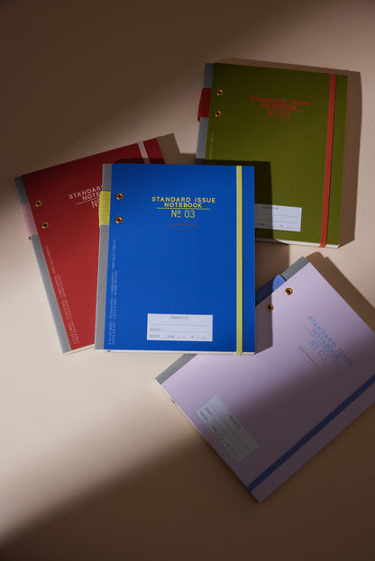 Four Standard Issue Planner Notebook No. 03 - Cobalt + Citron notebooks are arranged on a beige surface, their colorful covers and durable planner notebook design highlighted by soft lighting.