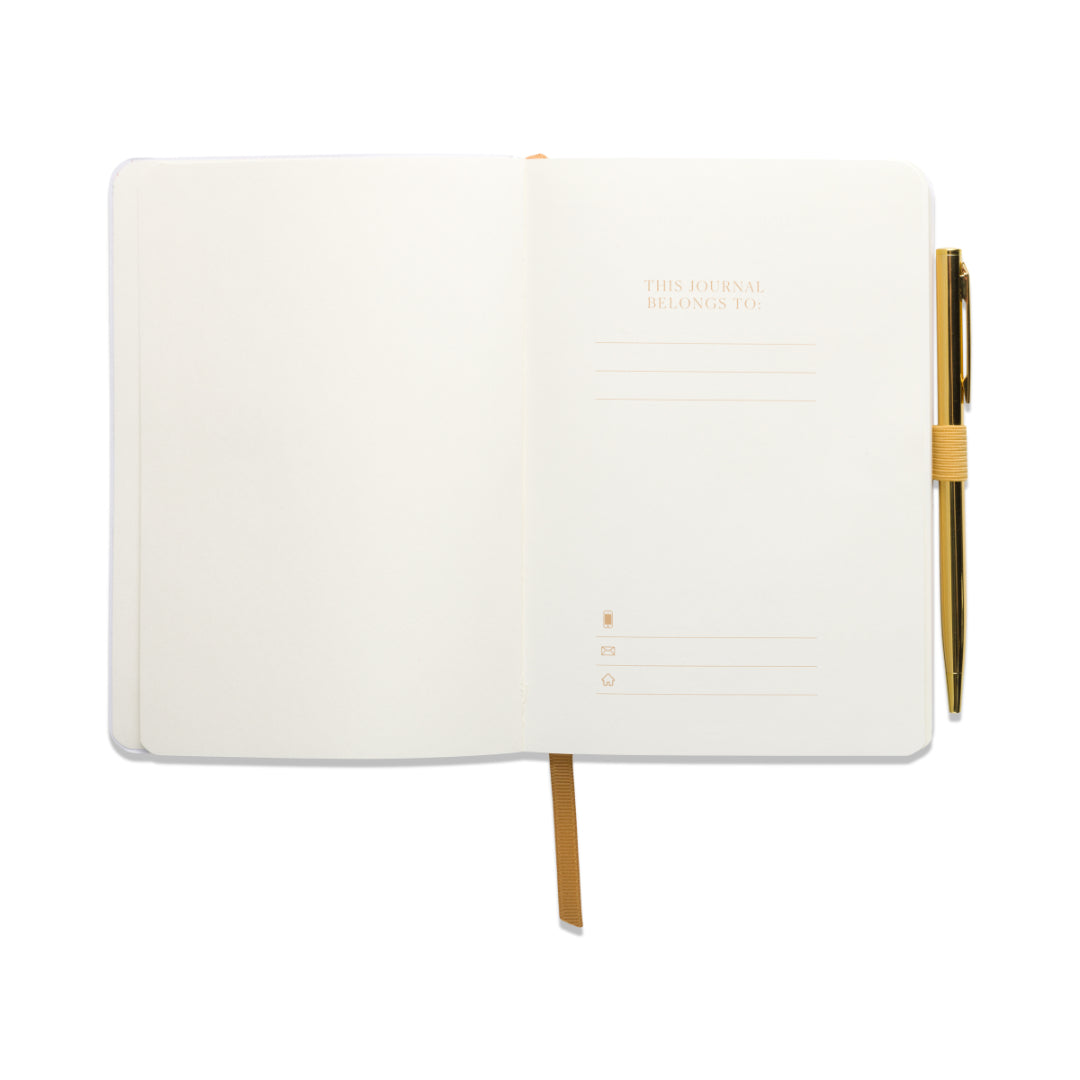 A Gratitude Journal with Pen - You Are Exactly Where You Need To Be, shown open with blank pages, featuring a golden pen attached on the right and a yellow ribbon bookmark. The left page is blank, while the right page reads “This journal belongs to:” with lines underneath for writing a name and details.