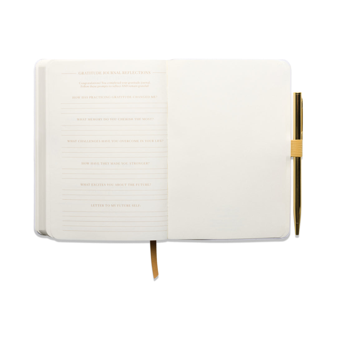 The “Gratitude Journal with Pen – You Are Exactly Where You Need To Be” features guided prompts on the left side of each spread and lined pages for writing on the right, accompanied by a gold pen secured in a loop and a yellow ribbon bookmark, all set against a white background.