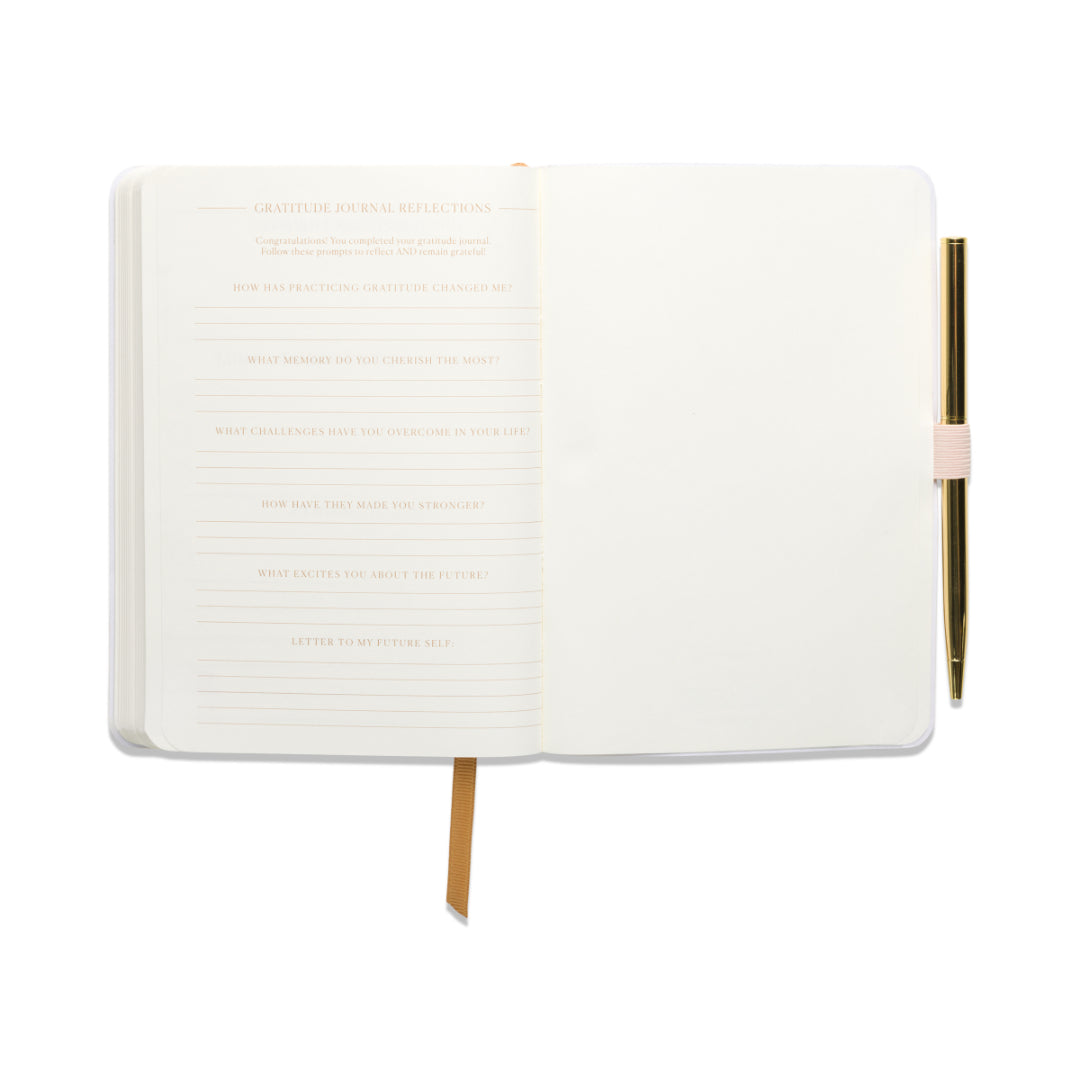 The Gratitude Journal with Pen - Pause is open to lined pages featuring reflection prompts, with a gold pen secured in the right-side loop and a ribbon bookmark draped across the pages. The journal rests against a white background.