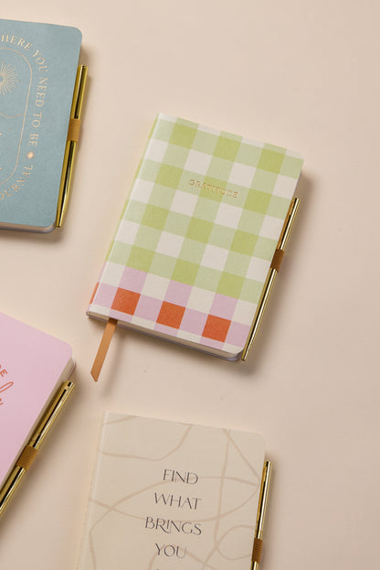 The Gratitude Journal with Pen – Picnic rests on a beige surface alongside other pastel guided journals, each designed for mindfulness and self-reflection. The checkered “GRATITUDE” journal features soothing colors and includes a gold pen.