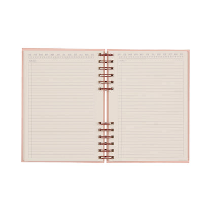The Standard Issue Planner Notebook No. 12 - Rosewood + Blush is shown open from above on a white background, revealing its lined pages with pink edges and labeled months at the top of each page, highlighting its high-quality construction and premium writing experience.