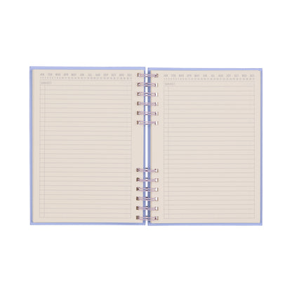 The Standard Issue Planner Notebook No. 12 - Lavender + Periwinkle is an open spiral-bound notebook with lined pages and a subject label at the top. The upper edges feature abbreviated months from January to December, making it ideal as a bullet journal or for everyday notes. Its blank, high-quality pages are designed for a premium writing experience.