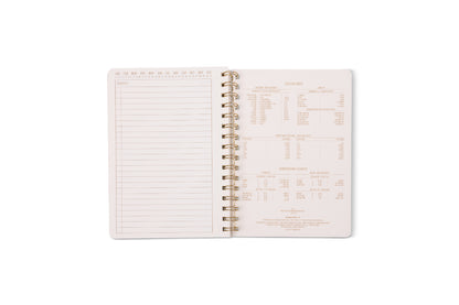 An open Tulip Twin Wire Notebook - Small Blue Lattice shows a blank lined notes page with perforations on the left and a kitchen measurement conversion chart with various units and equivalents on the right.