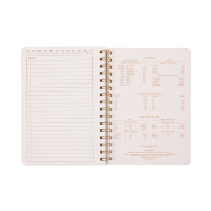 An open Tulip Twin Wire Notebook - Small Green Lattice reveals a blank lined page on the left and a kitchen measurement conversion chart on the right. The background is light, featuring subtly printed text in pale tones, while delicate botanical accents lend an elegant touch.