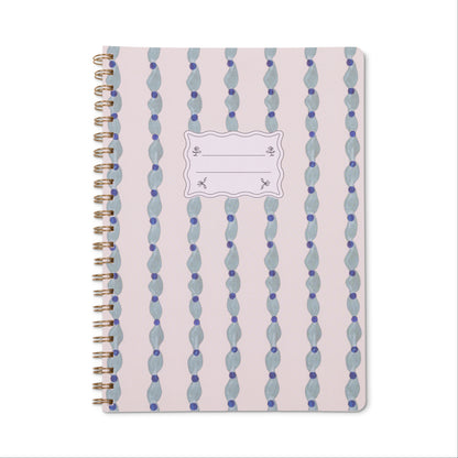 The Tulip Twin Wire Notebook - Large Wavy Blue features a light pink cover with wavy blue, green, and purple dotted patterns, a white name label, lined perforated pages, and sturdy twin-wire binding for convenient note-taking.