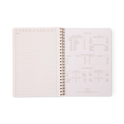 An open Tulip Twin Wire Notebook - Large Wavy Blue reveals a blank lined perforated page on the left and cooking measurement conversion charts on the right, all securely bound within the twin-wire design for convenient flipping and note-taking.