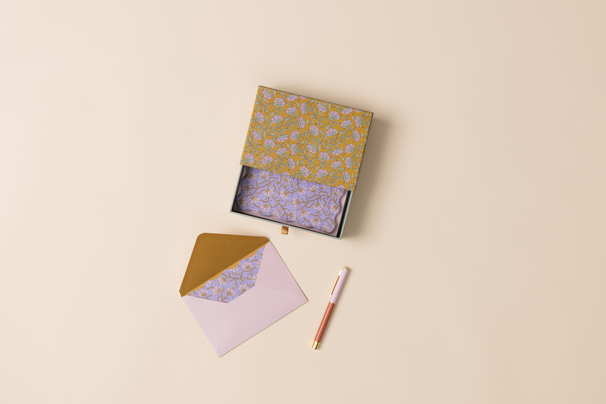 Notebook with a patterned cover, matching envelope, and pen on a beige background